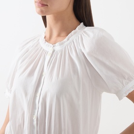 Model wearing Paige white cotton dress, close-up of gathered frill neckline and short puff sleeves with button front detail