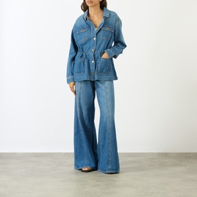 Model wearing Paige denim jacket in La Verne blue with cinched waist, styled with matching wide-leg flare jeans.