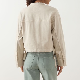 Model wearing Paige jacket in Vintage Biscotti, back view, showing tie-detail cuffs and relaxed cotton fit, styled with sage green jeans.