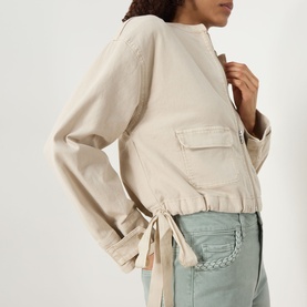 Model wearing Paige jacket in Vintage Biscotti, cotton blend with chest pocket, tie-hem detail and wide cuffs, styled with light blue jeans.
