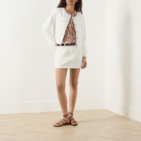 Model wearing Paige Toasted Ecru denim mini skirt with matching jacket, floral top and brown strappy flat sandals.