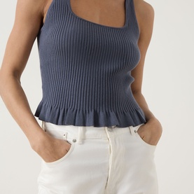 Model wearing Paige Pacific Blue ribbed knit tank with frill hem, styled with white wide-leg trousers.