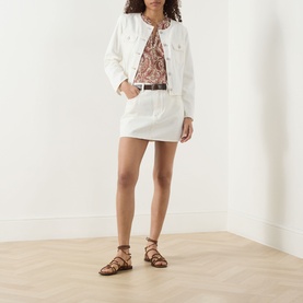 Model wearing Paige silk top in Antique White Multi print, styled with white denim jacket and mini skirt, brown belt and strappy sandals.