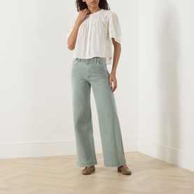 Model wearing Paige Ivory cotton top with flutter sleeves, styled with wide-leg sage green trousers and brown mules