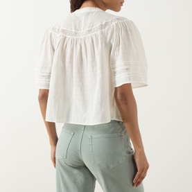 Model wearing Paige ivory cotton top with lace trim detailing and puff sleeves, styled with sage green jeans, seen from behind.