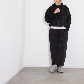 Model wearing Robyn Lynch black cotton casual jacket with hood and zip, styled with matching black trousers and grey trainers.