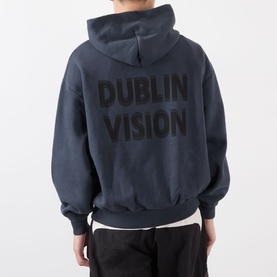 Model wearing Robyn Lynch slate blue cotton hoodie, back view showing large Dublin Vision logo print, styled with black trousers