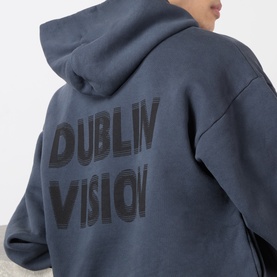 Model wearing Robyn Lynch slate blue cotton hoodie, rear view showing tonal Dublin Vision graphic print across back