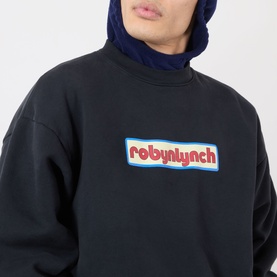 Model wearing Robyn Lynch off black sweatshirt with chest logo patch, styled with a navy blue hoodie underneath.