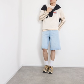 Model wearing Robyn Lynch Logo Graphic T-Shirt in off white with striped long-sleeve underlayer, light blue denim shorts and gold trainers.