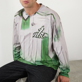 Model wearing Robyn Lynch green long-sleeve graphic jersey T-shirt with printed stripe and logo detail, styled with dark trousers and chain necklace.