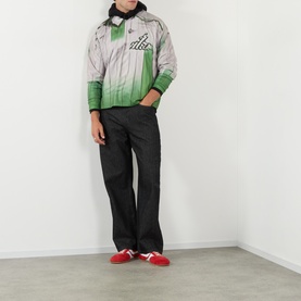 Model wearing Robyn Lynch green and grey ombre zip-up jacket with black trousers and red trainers.
