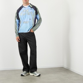 Model wearing Robyn Lynch blue long-sleeve graphic T-shirt with striped sleeves, styled with black wide-leg trousers and silver trainers.
