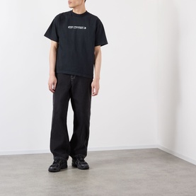 Model wearing Robyn Lynch Skint Logo T-Shirt in off black with crew neck, styled with black wide-leg trousers and black chunky trainers.