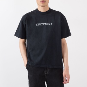 Model wearing Robyn Lynch Skint Logo T-Shirt in off black with high crew neck, dropped shoulders, and front logo graphic, styled with blue jeans.