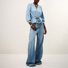 Model wearing Bash blue denim belted wrap blouse with puff sleeves, styled with wide-leg light wash jeans