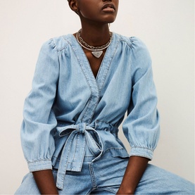 Model wearing Bash blue denim wrap top with puff sleeves and tie waist, styled with matching blue denim jeans and silver layered necklaces