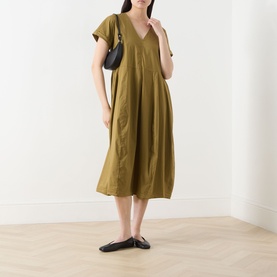 Model wearing Transit Pleated Pocket Dress in olive, V-neckline, short sleeves, midi length, styled with black bag and flat shoes