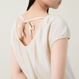 Model wearing Transit Textured Pocket Dress in sand, showing V-back neckline with self-tie ribbon fastening and short sleeves