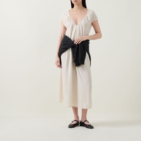 Model wearing Transit Textured Pocket Dress in sand, V-neckline, short sleeves, midi length, styled with a black jacket and black flat shoes.
