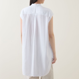 Model wearing Transit Patch Pocket Blouse in white, back view showing box pleat detail, cap sleeves and curved longline hemline