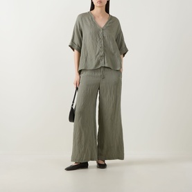 Model wearing Transit green crinkle V-neck shirt with matching wide-leg trousers, styled with black bag and flat shoes.
