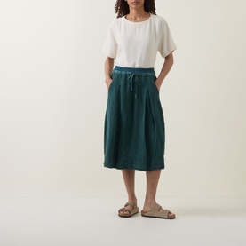 Model wearing Transit petrol linen midi skirt with drawstring waist, styled with white top and tan sandals