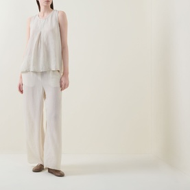 Model wearing Transit Pleated Textured Blouse in sand, sleeveless with inverted front pleats, styled with wide-leg cream trousers and taupe flats.