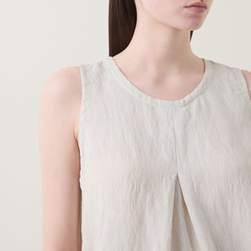 Model wearing Transit Pleated Textured Blouse in sand, showing round neckline, sleeveless cut and front inverted pleat detail.