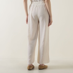 Model wearing Transit sand wide-leg trousers, rear view, styled with beige flat mules. Relaxed fit with elasticated waistband.