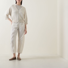 Model wearing Transit Cropped Barrel Leg Trousers in sand linen, styled with a cream V-neck cardigan and taupe flat shoes.