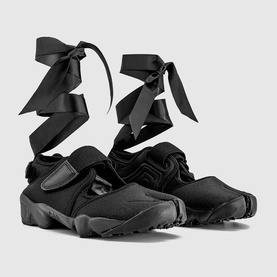 Nike black canvas trainers with velcro strap, rugged rubber sole, and long black satin ribbon ankle ties