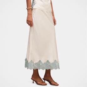 Model wearing Forever New champagne midi skirt with sage green lace hem trim, styled with matching top and strappy heeled sandals.