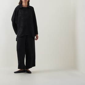 Model wearing Annette Gortz black viscose blouse with oversized fit, styled with wide-leg black trousers and flat shoes.