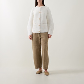 Model wearing Annette Gortz white cardigan with gold buttons, styled with khaki tapered trousers and beige flat mules.
