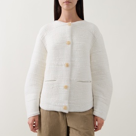 Model wearing Annette Gortz white textured knit cardigan with large wooden buttons and patch pockets, styled with khaki trousers.