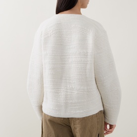 Model wearing Annette Gortz white cardigan, textured knit, shown from behind, styled with khaki trousers