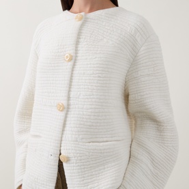 Model wearing Annette Gortz white cardigan in textured knit with cream button fastening, styled with khaki trousers.