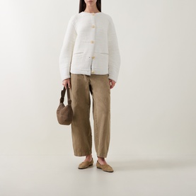 Model wearing Annette Gortz white cardigan with textured knit and gold buttons, styled with khaki trousers and beige flats, carrying brown bag.