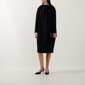 Model wearing Annette Gortz black dress with gathered neckline and long sleeves, styled with black heels and clutch bag.
