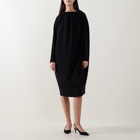 Model wearing Annette Gortz black dress with gathered neckline, long sleeves and cocoon silhouette, styled with black heels.