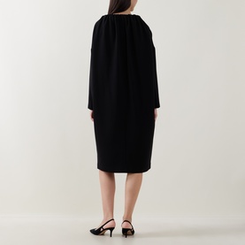 Model wearing Annette Gortz black dress, back view, showing gathered neckline and long sleeves, styled with black slingback heels.