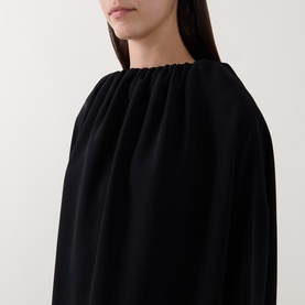 Model wearing Annette Gortz black dress with gathered ruched neckline and relaxed wide sleeves in fluid fabric.