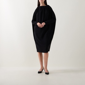 Model wearing Annette Gortz black dress with dramatic cape-like sleeves and gathered neckline, styled with black ballet flats