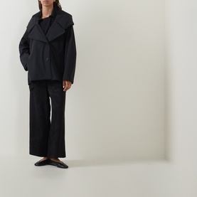 Model wearing Annette Gortz black cotton jacket with wide lapels, styled with matching wide-leg trousers and black ballet flats.