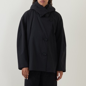 Model wearing Annette Gortz black cotton jacket with attached hood, double-button front fastening, styled with wide-leg black trousers.