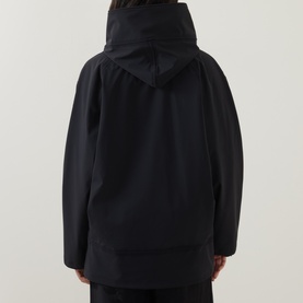 Model wearing Annette Gortz black hooded jacket, rear view, oversized fit in 100% cotton fabric.