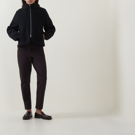 Model wearing Annette Gortz black cotton jacket with zip fastening and funnel neck, styled with dark slim trousers and loafers.
