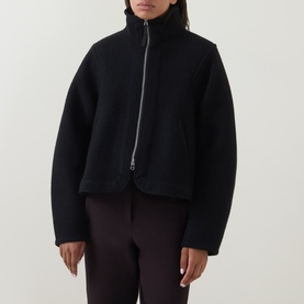 Model wearing Annette Gortz black cotton zip-up jacket with high funnel neck and oversized silhouette, styled with dark trousers.