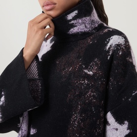 Model wearing Annette Gortz merino wool turtleneck knitwear in Still Dust abstract black, lilac and white pattern, close-up view
